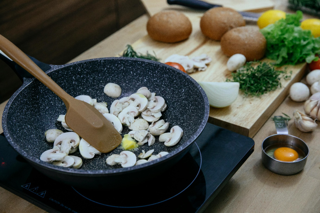 A silicone spatula being used to cook mushrooms in a pan